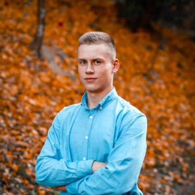 man in blue dress shirt standing on brown leaves during daytime